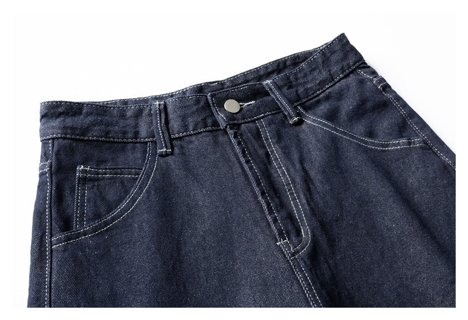 Close-up of dark indigo jeans showing the waistband, button, fly, belt loops, and curved front pocket.