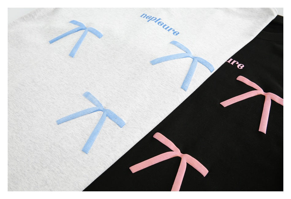 Close-up of light gray and black garments with repeated blue and pink bow motifs and small printed lettering.