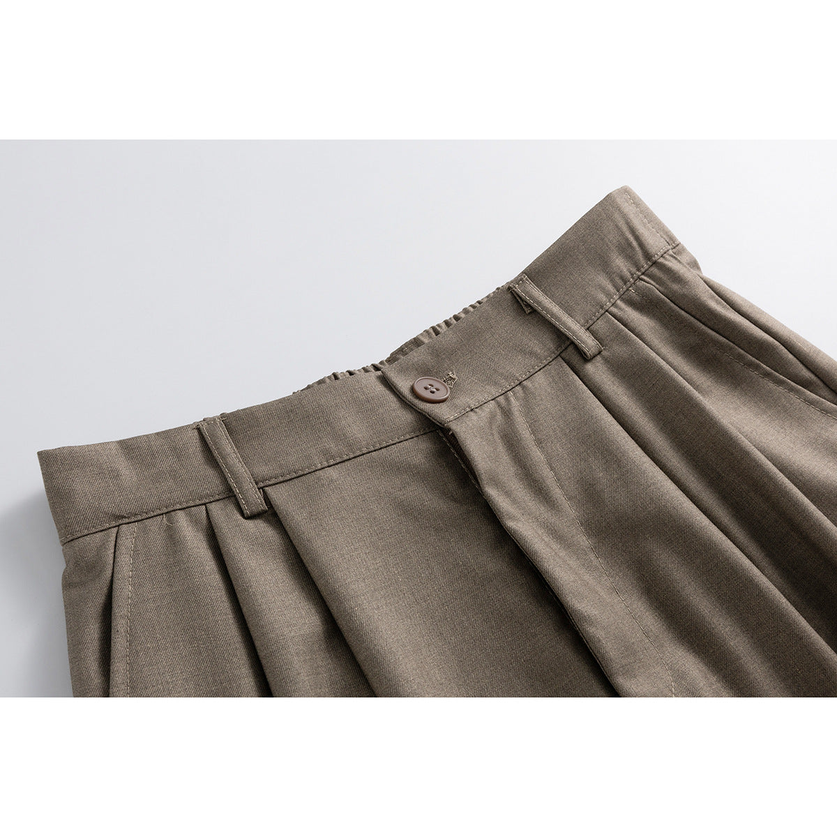 Close-up of taupe shorts showing the waistband, button, belt loops, pleats, and front fly.
