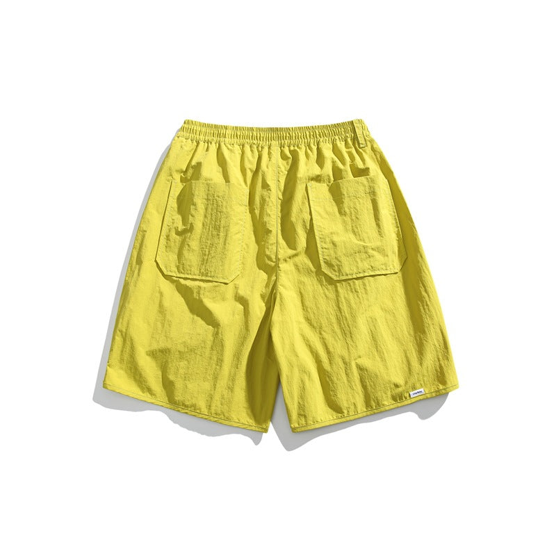Back view of bright yellow shorts with an elastic waistband and two large rear patch pockets, on a white background.