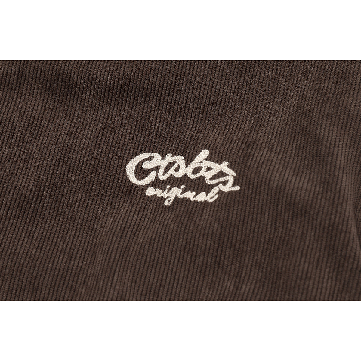 Close-up of small white script embroidery on brown ribbed jacket fabric.