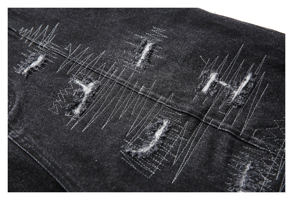 Close-up of black denim shorts with distressed slashes and dense contrasting stitched patterns.