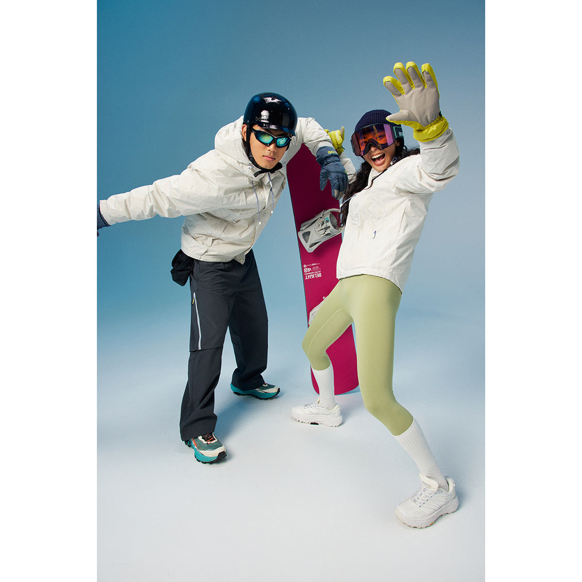 Two snowboarders wear white jackets; one pairs hers with light green leggings, while he wears dark pants.