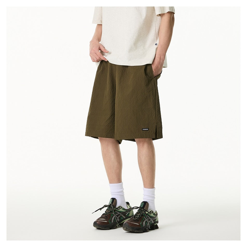 Front angled view of a model wearing olive textured knee-length shorts with a light T-shirt and sneakers.