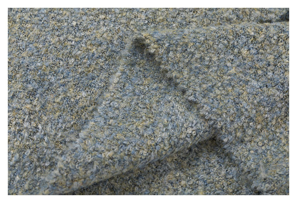 Close-up of a fuzzy, looped knit in mottled gray-blue and beige, folded to show its textured surface.