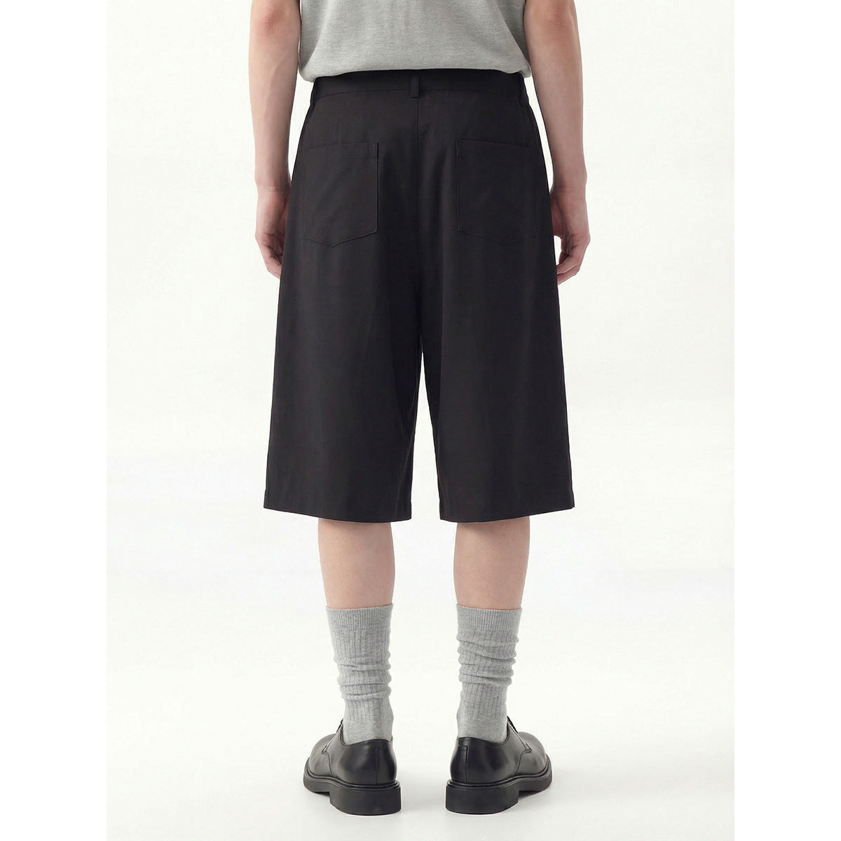 Rear view of a model wearing black knee-length shorts with two back patch pockets.