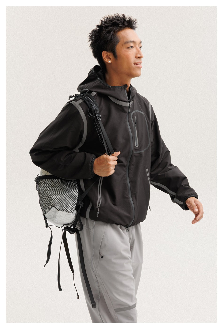 Close view of a model wearing a black hooded jacket with gray piping, zip pockets, and light gray trousers.
