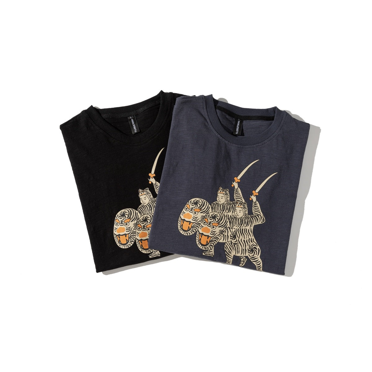 Black and charcoal T-shirts folded to show their matching cream-and-orange tiger-rider front graphics.