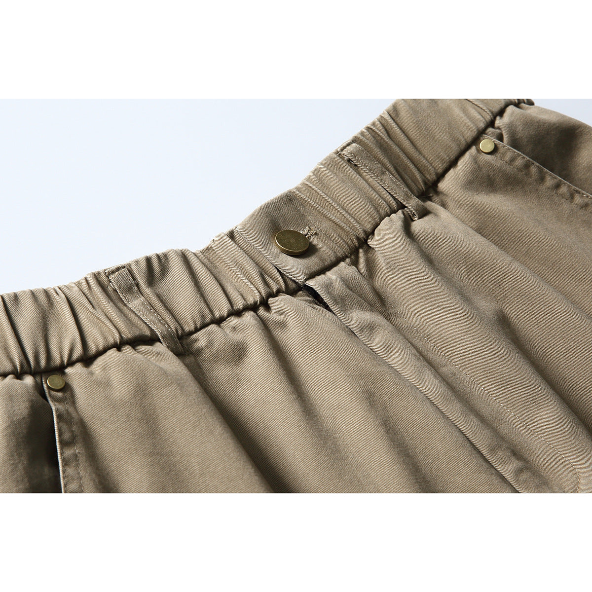 Close-up of taupe cargo trousers showing an elastic waistband, belt loop, and metal buttons.