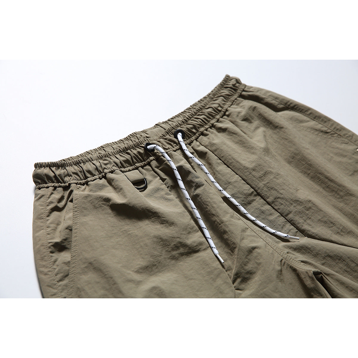 Close-up of taupe shorts with an elastic waistband, white drawstrings, and a small black D-ring.