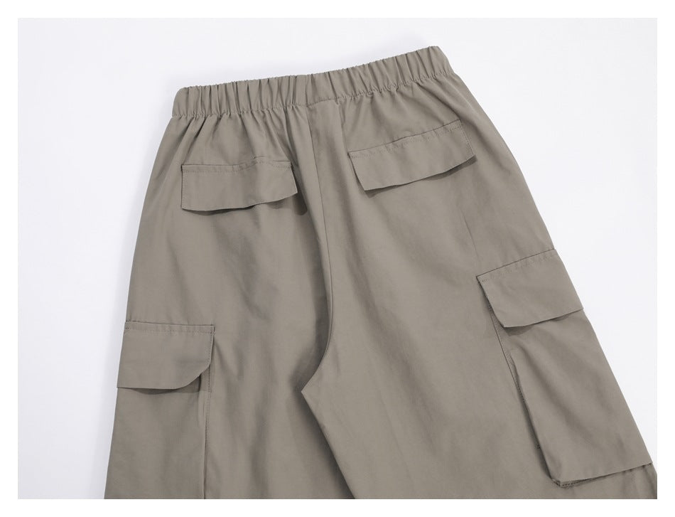 Back view of taupe cargo pants laid flat, with an elastic waist and multiple flap pockets.