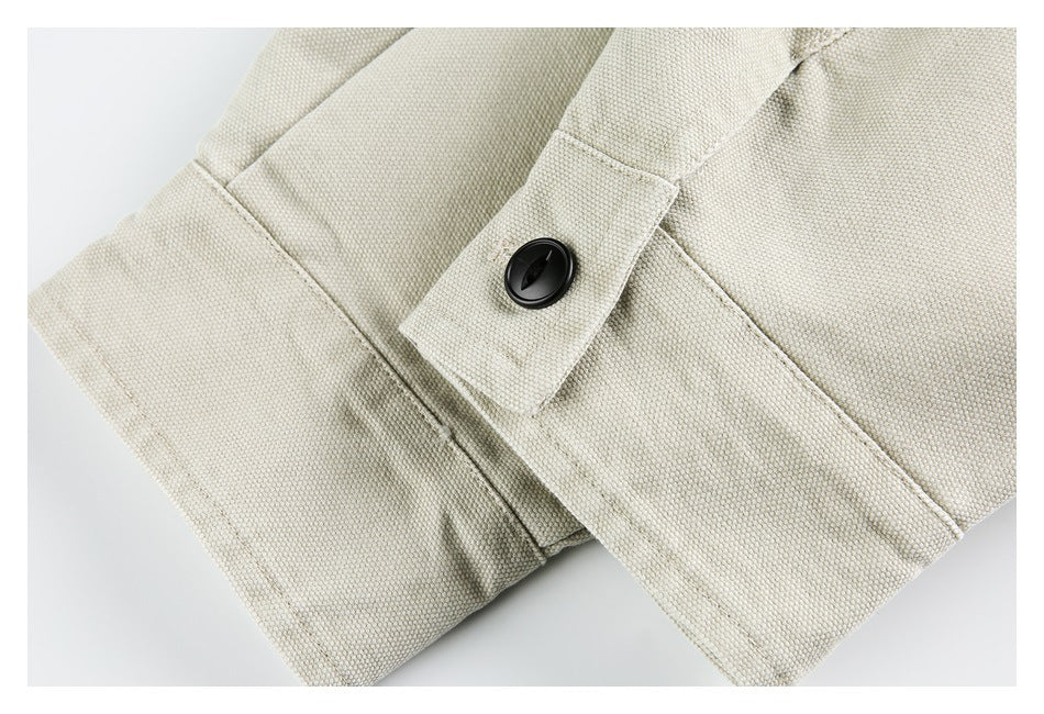 Close-up of a black button on a tab of light beige fabric with visible stitching.