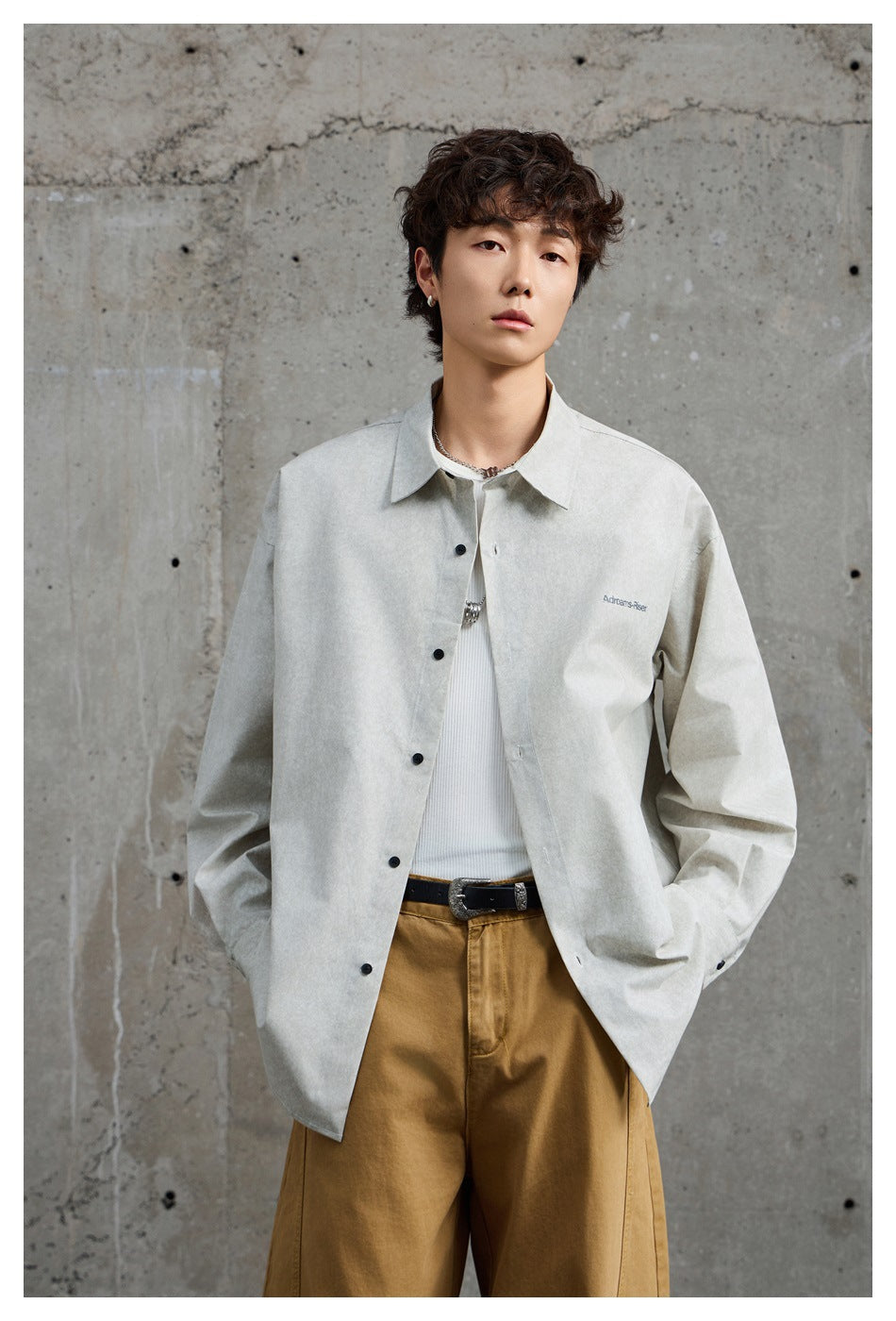 Model wearing an open light gray oversized button-up shirt over a white top and brown trousers.