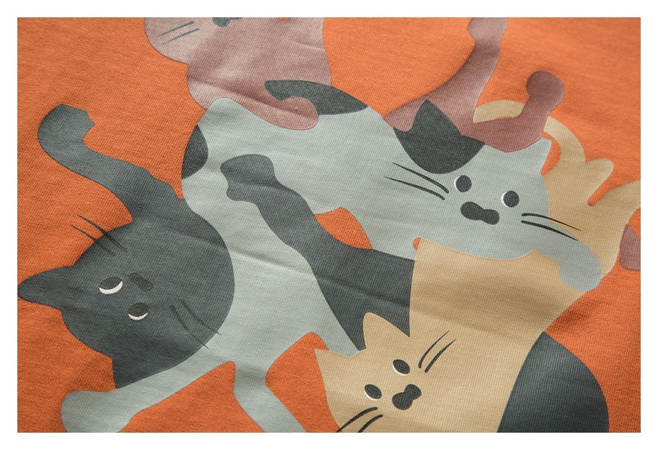 Close-up of an orange garment printed with overlapping cartoon cats in gray, cream, and muted pink.
