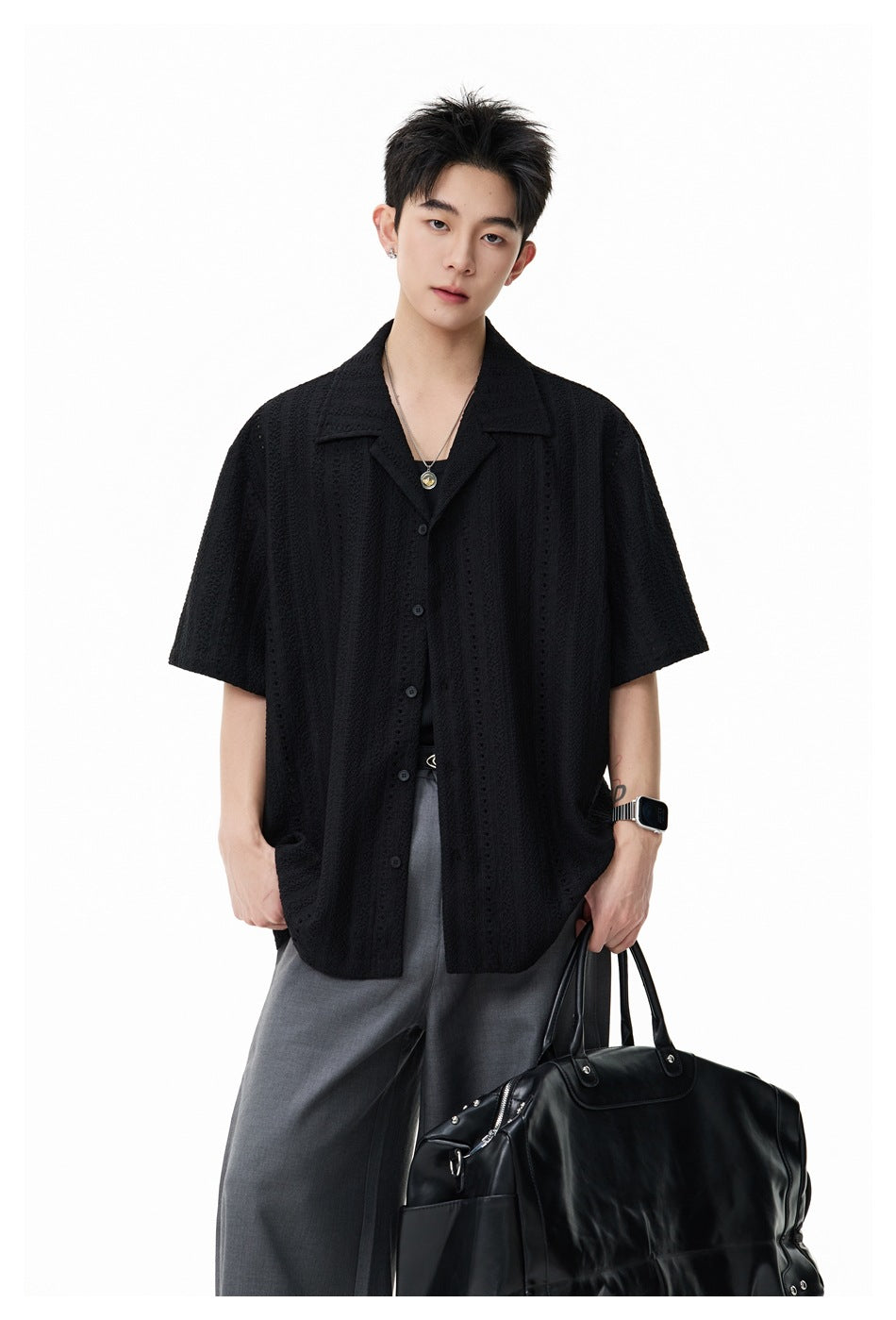Front view of a model wearing a black textured short-sleeve button-up shirt with a wide collar.