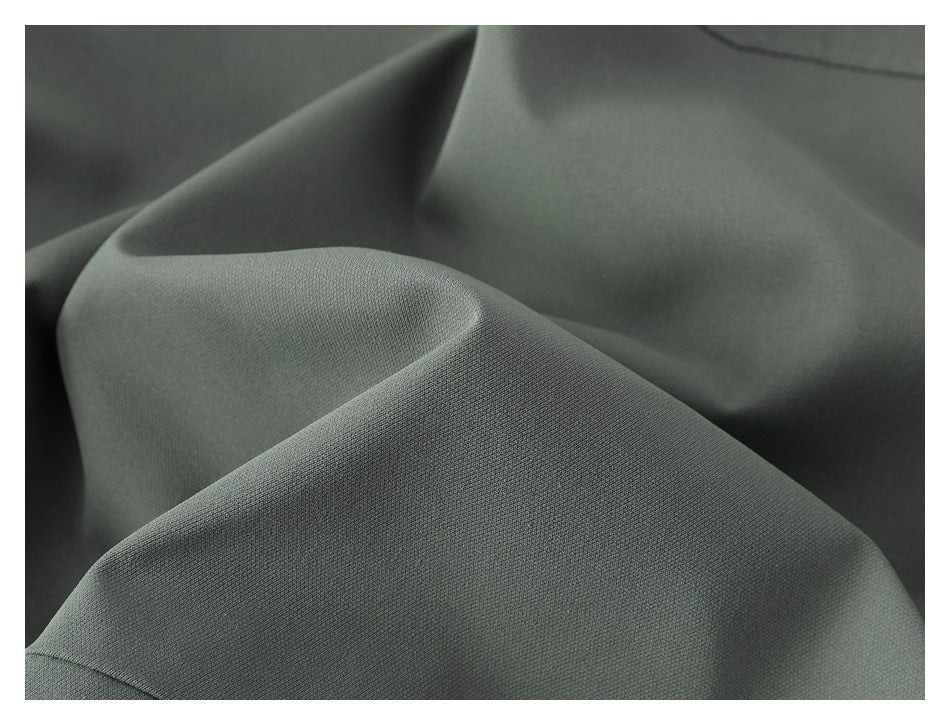 Close-up of muted gray-green garment fabric in soft folds, with a visible stitched seam.