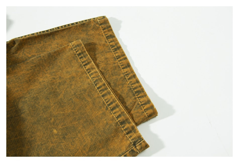 Close-up of the ochre-brown pants' stitched leg hems laid flat on a white background.