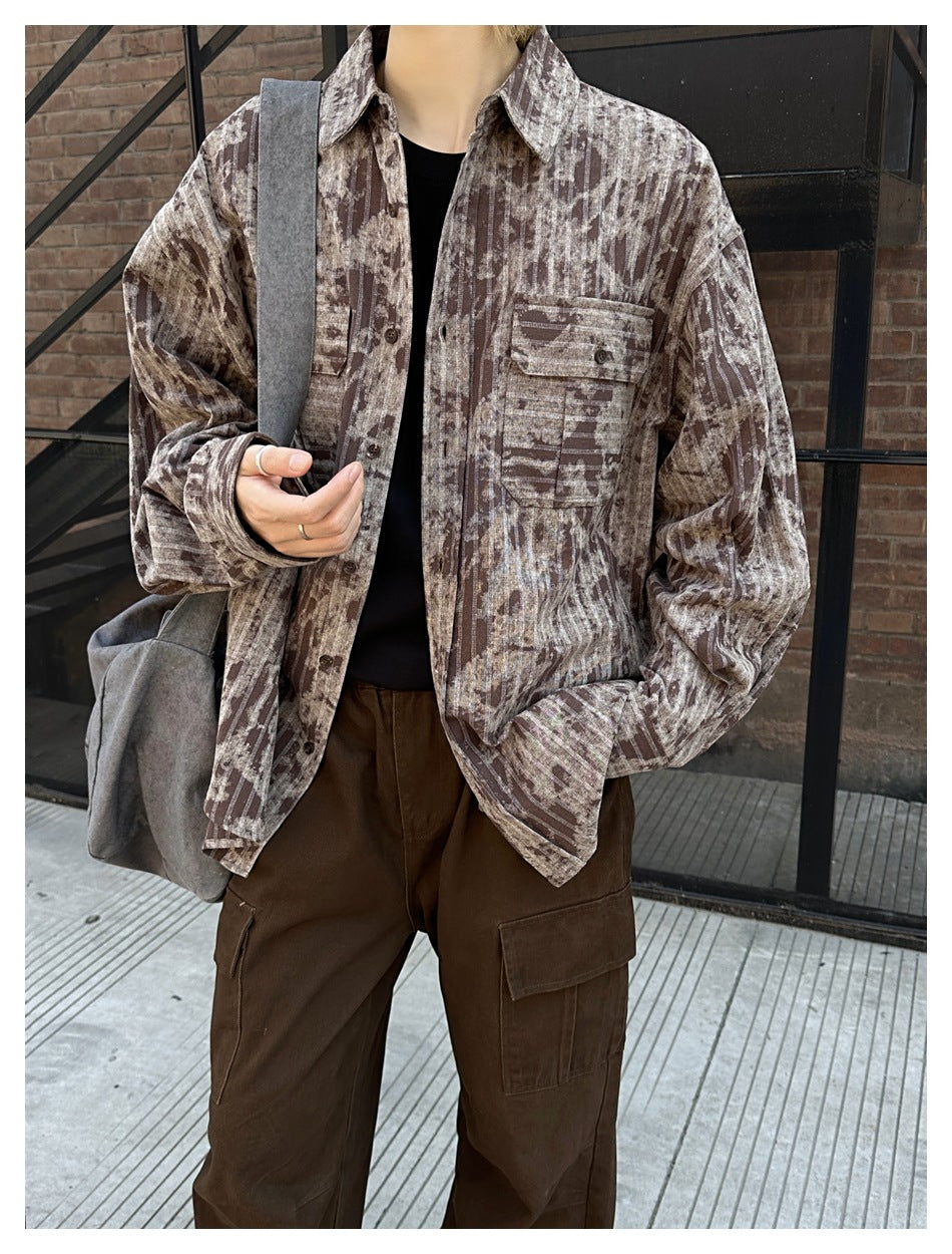 Close crop of a model wearing a brown and beige abstract-stripe button-up shirt with flap chest pockets and dark cargo pants.