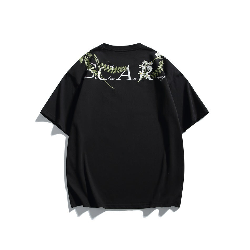 Back of black T-shirt with embroidered lettering, green leaves and white flowers across the upper back