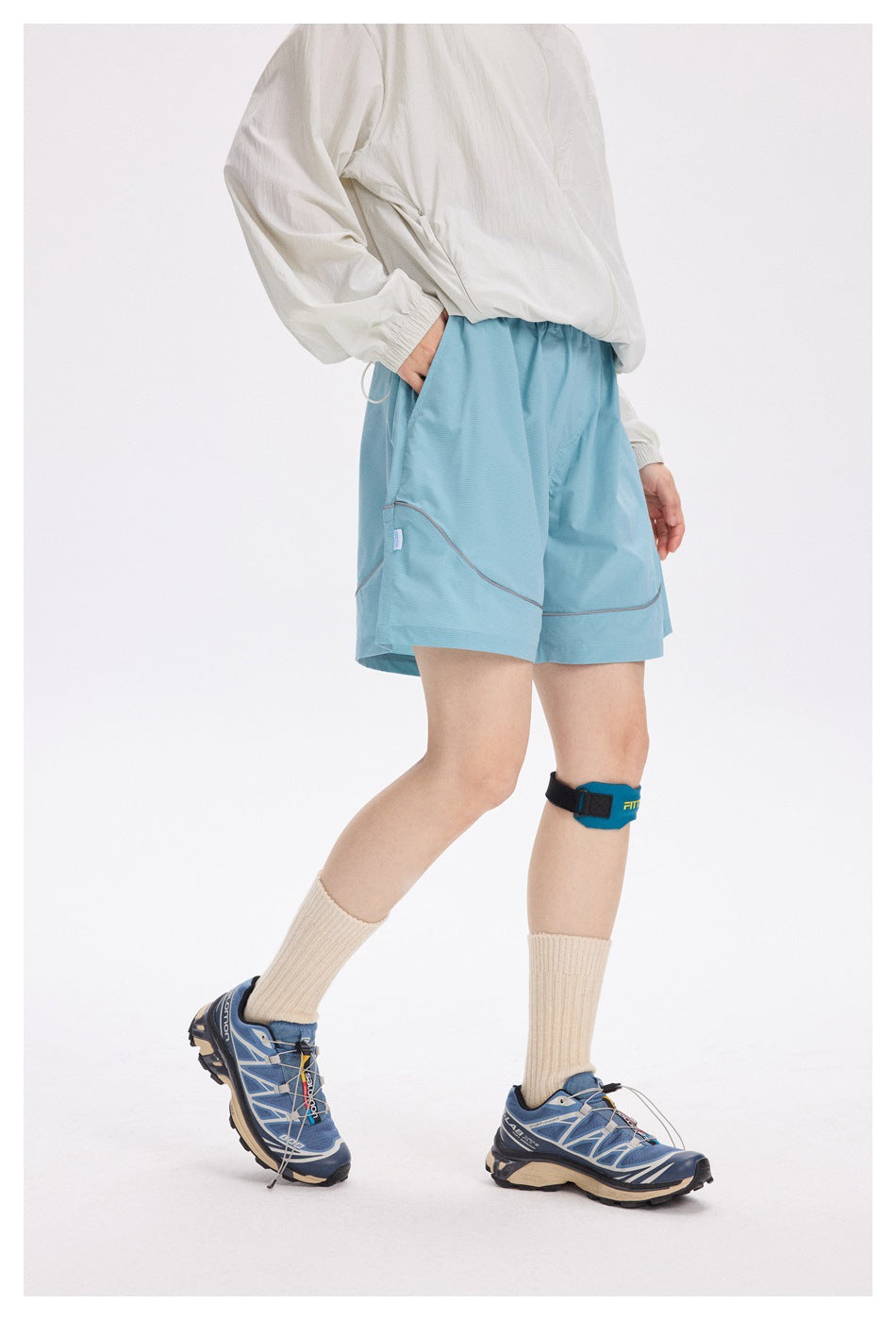 Person in a side pose wearing light aqua athletic shorts with curved contrast piping and a white top.