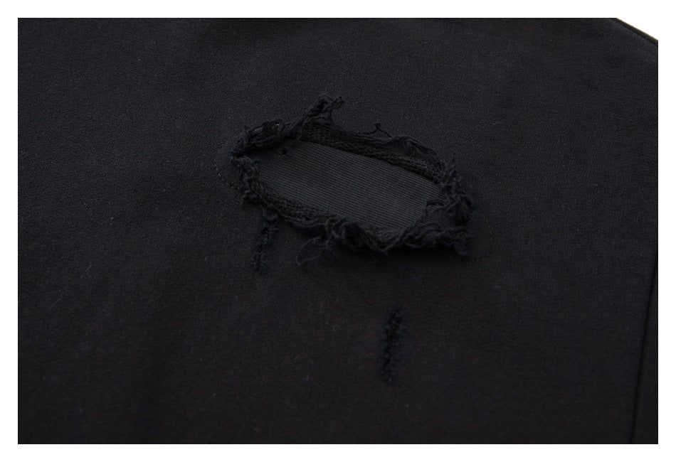 Close-up of a black garment with a frayed oval tear and dark fabric backing.