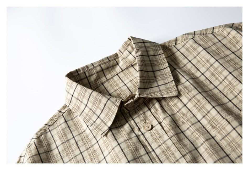Close-up of the pointed collar and upper button placket of a beige plaid shirt.