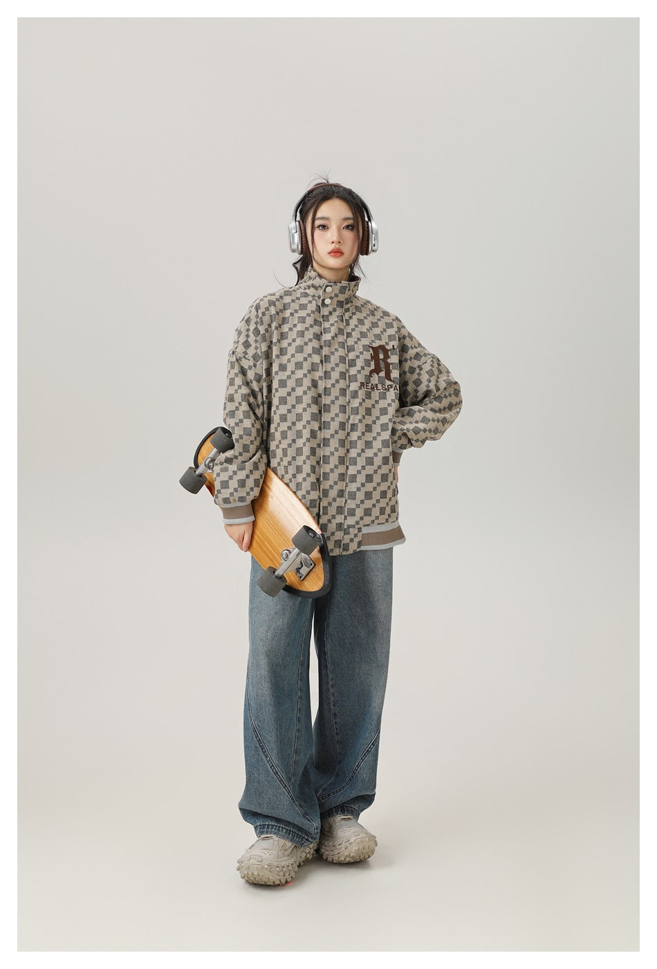 Model wearing a zipped checkered stand-collar jacket with wide-leg jeans, holding a skateboard and wearing headphones