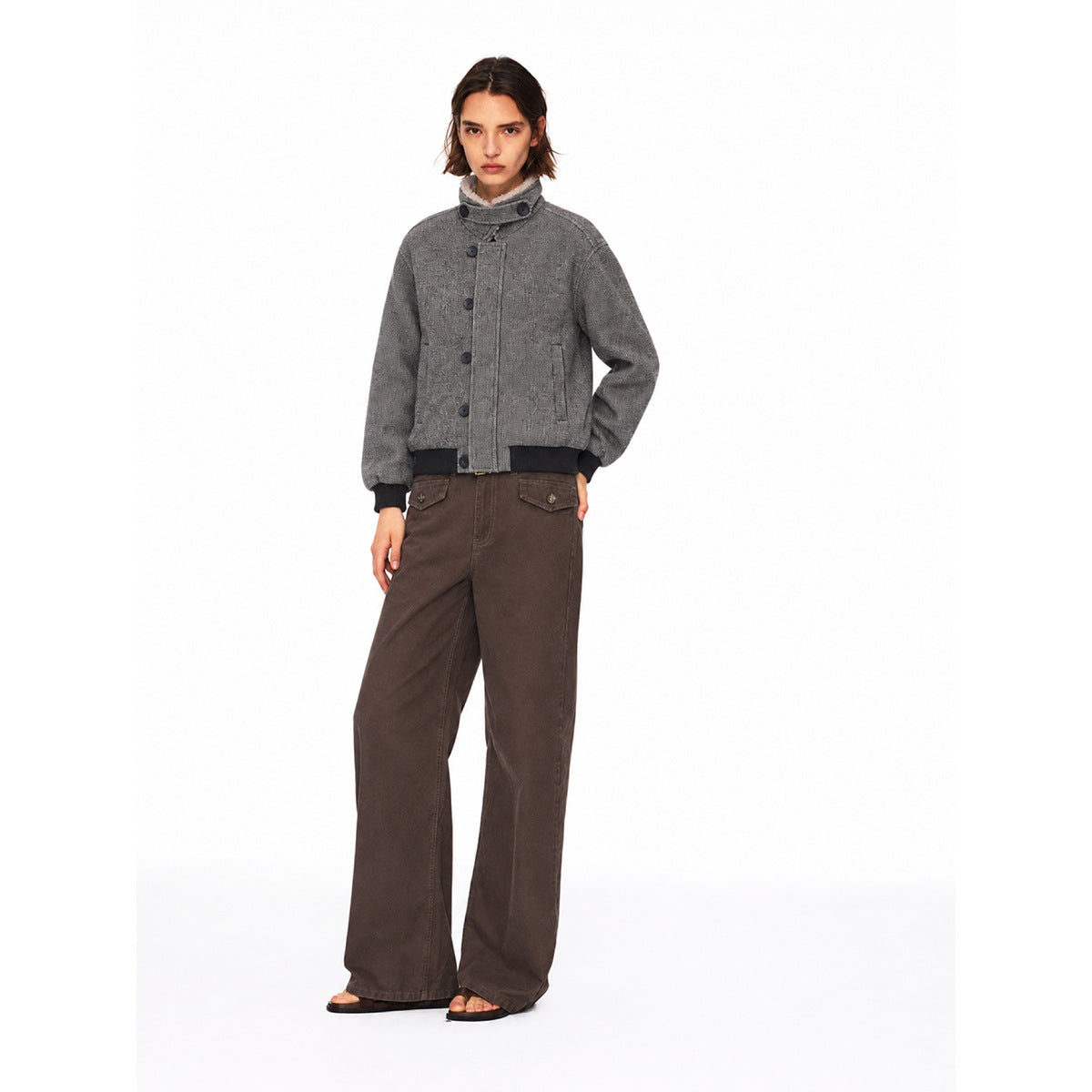 Front view of a model in a gray high-collar button jacket with black ribbed trim and wide-leg brown pants.