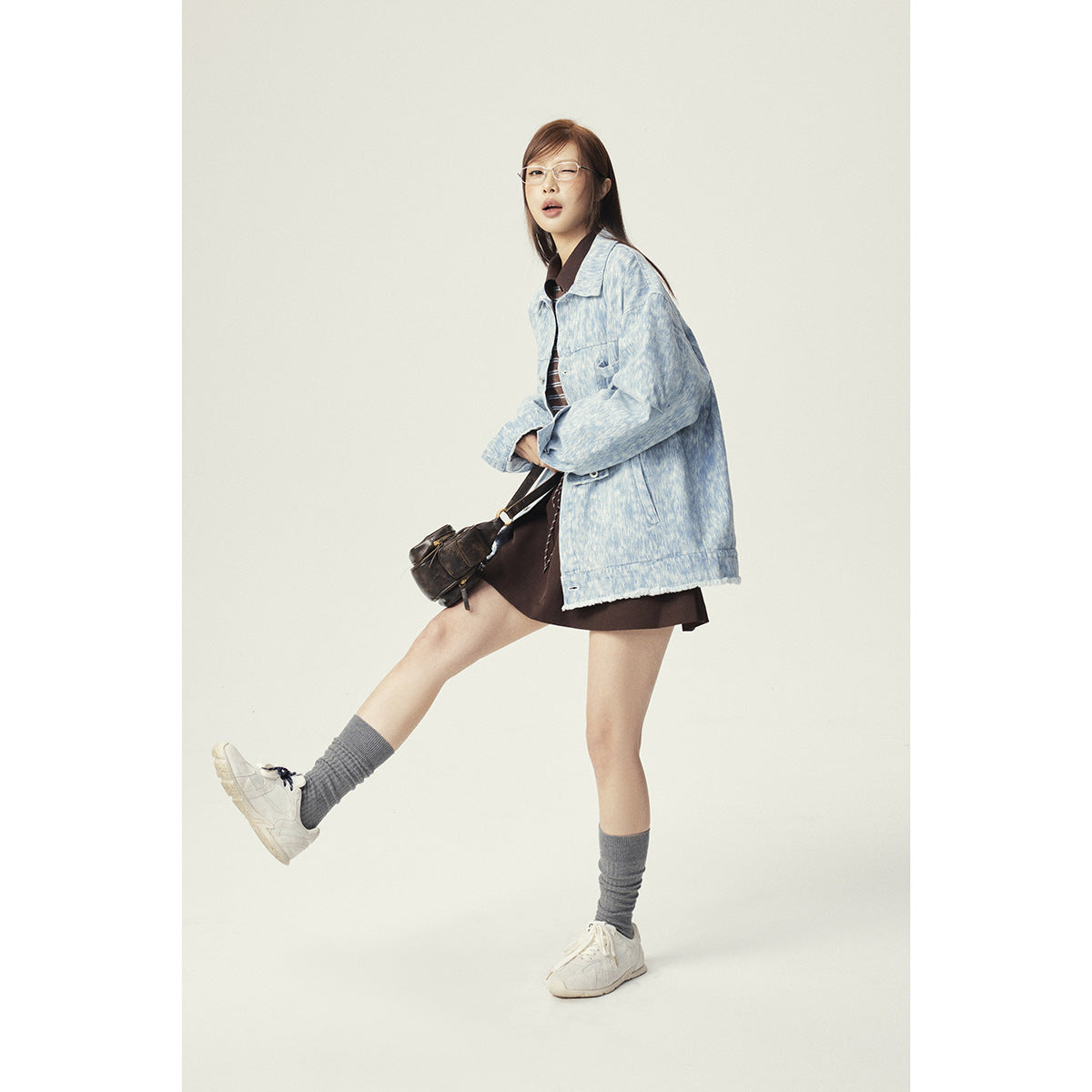 Model wearing an oversized pale blue mottled button-front jacket with a dark skirt, shown at a three-quarter angle.