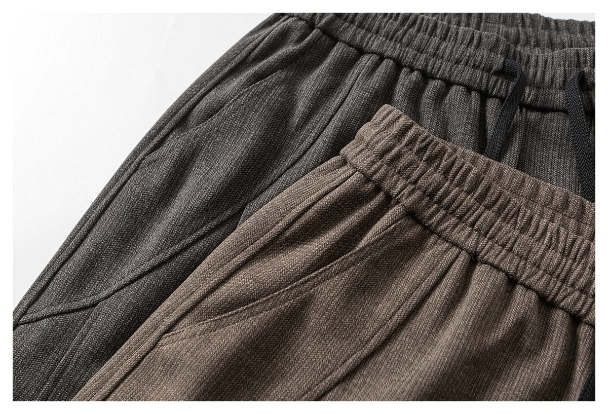 Close-up of two pairs of textured elastic-waist trousers in charcoal gray and taupe.