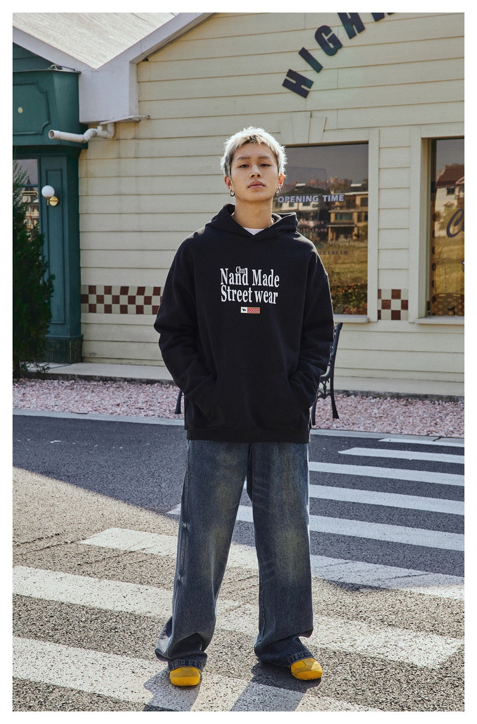 Model wearing a black graphic hoodie with hands in the front pocket, paired with wide-leg jeans and yellow shoes