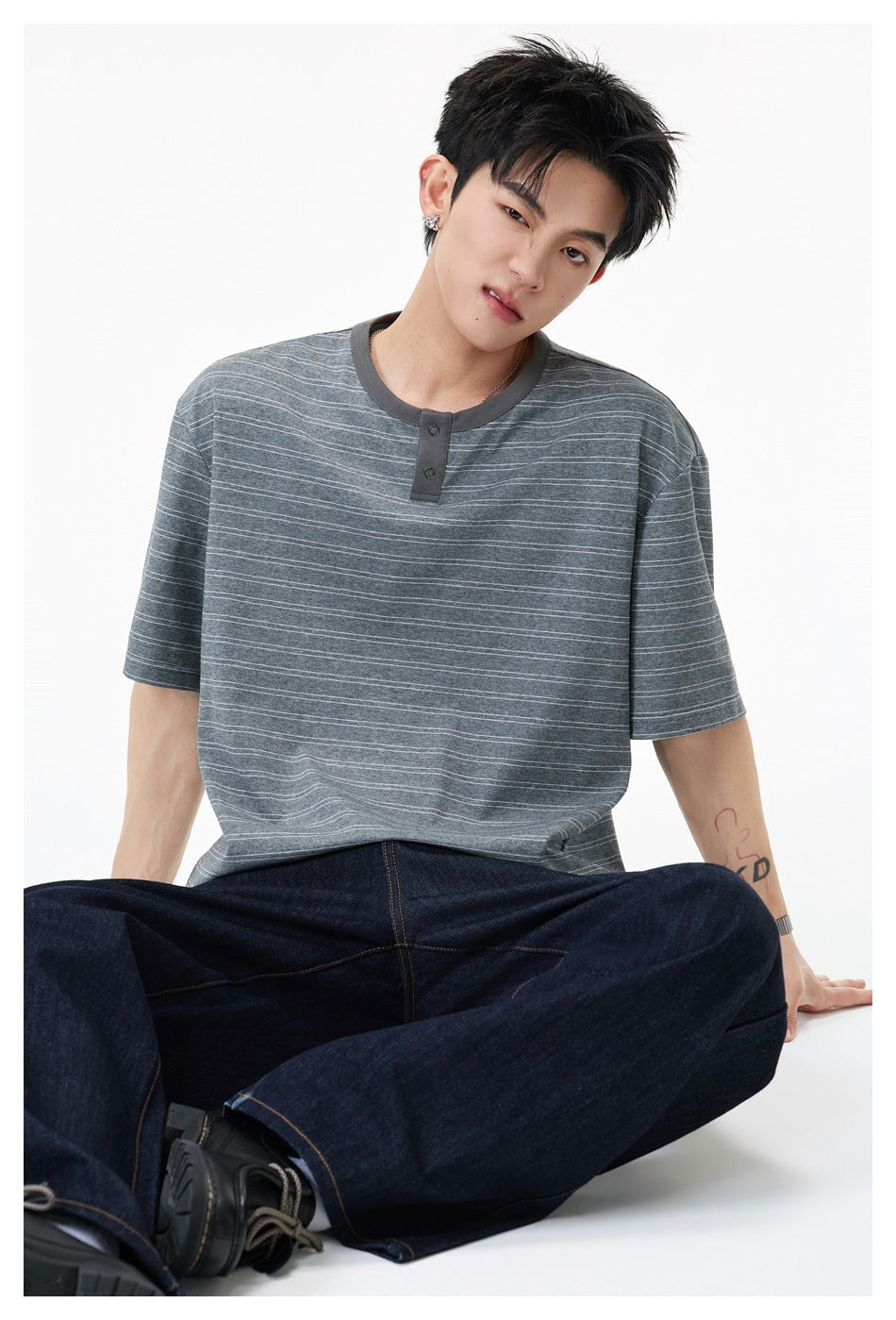 Seated model wearing a gray striped Henley with a dark button placket; close view of the shirt.