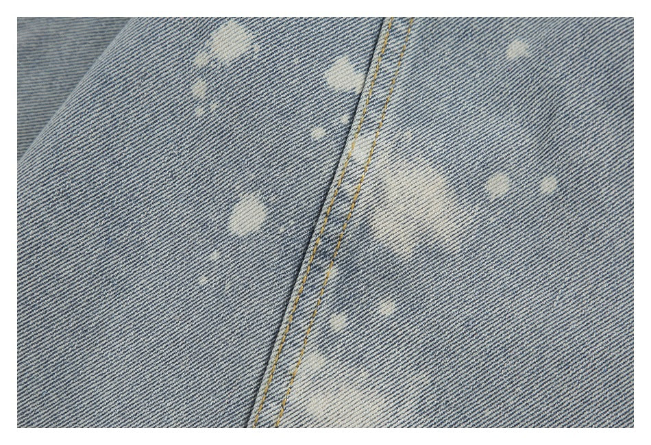 Close-up of light blue acid-wash denim with pale irregular marks and parallel tan-stitched seams.