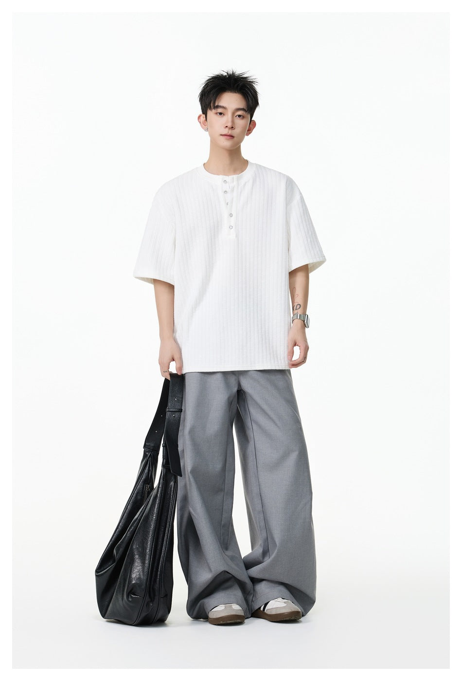 Model wearing a white short-sleeve ribbed Henley shirt with a button placket and gray wide-leg trousers, carrying a black