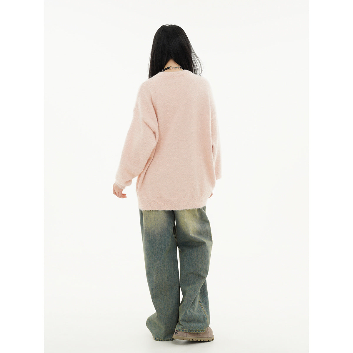 Back view of a model wearing an oversized pale pink sweater with loose green-gray jeans.