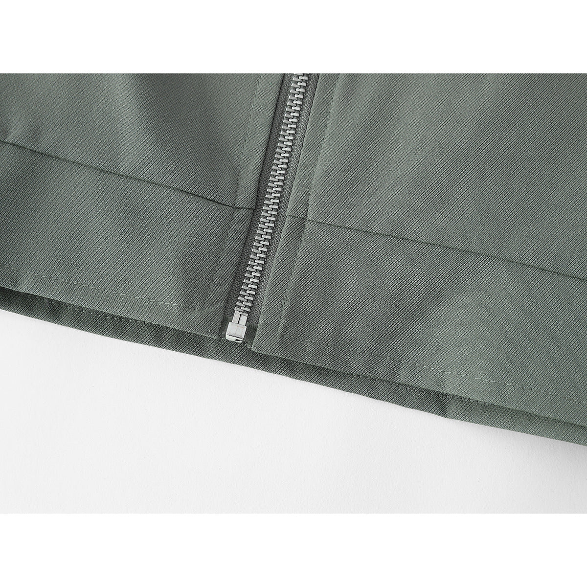 Close-up of the gray-green jacket's lower front, showing the zipper, stitched panels, and hem.