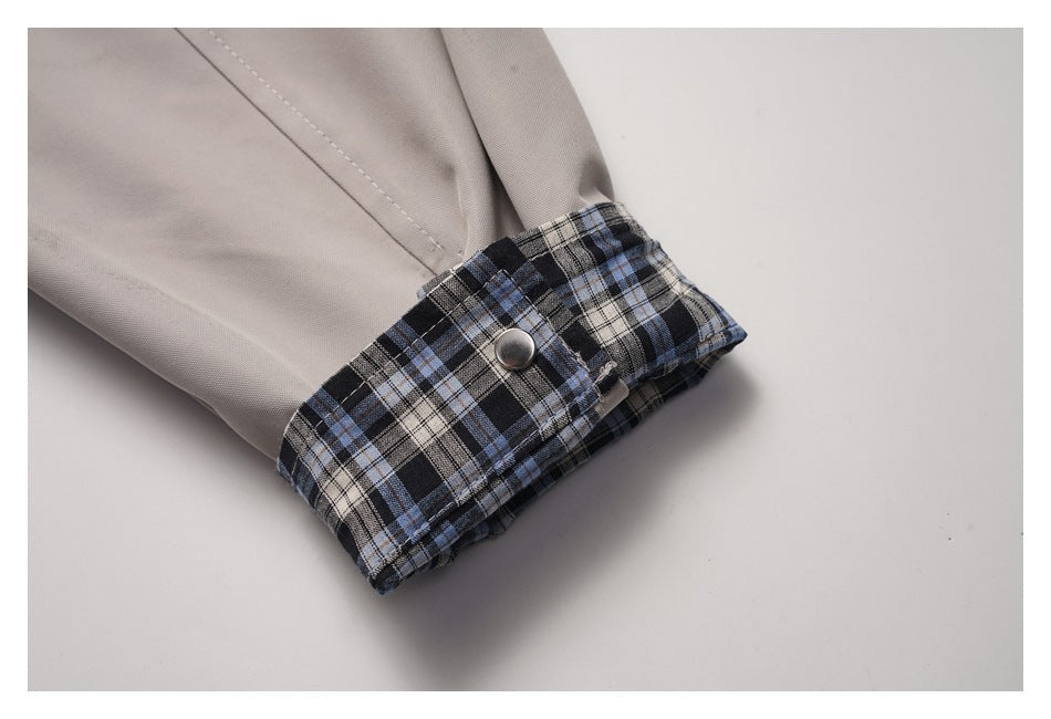 Close-up of a light taupe jacket cuff with blue, black, and cream plaid lining and a metal snap.