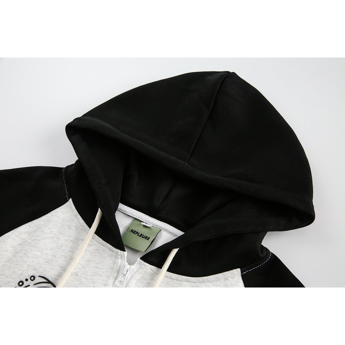 Close-up of a black hood and shoulders on a heather light-gray zip hoodie, with cream drawstrings and partial black artwork.