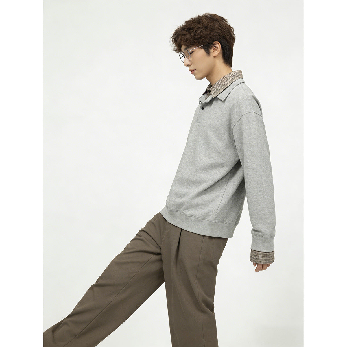 Side view of a model wearing a light gray collared pullover with plaid details and loose taupe trousers.