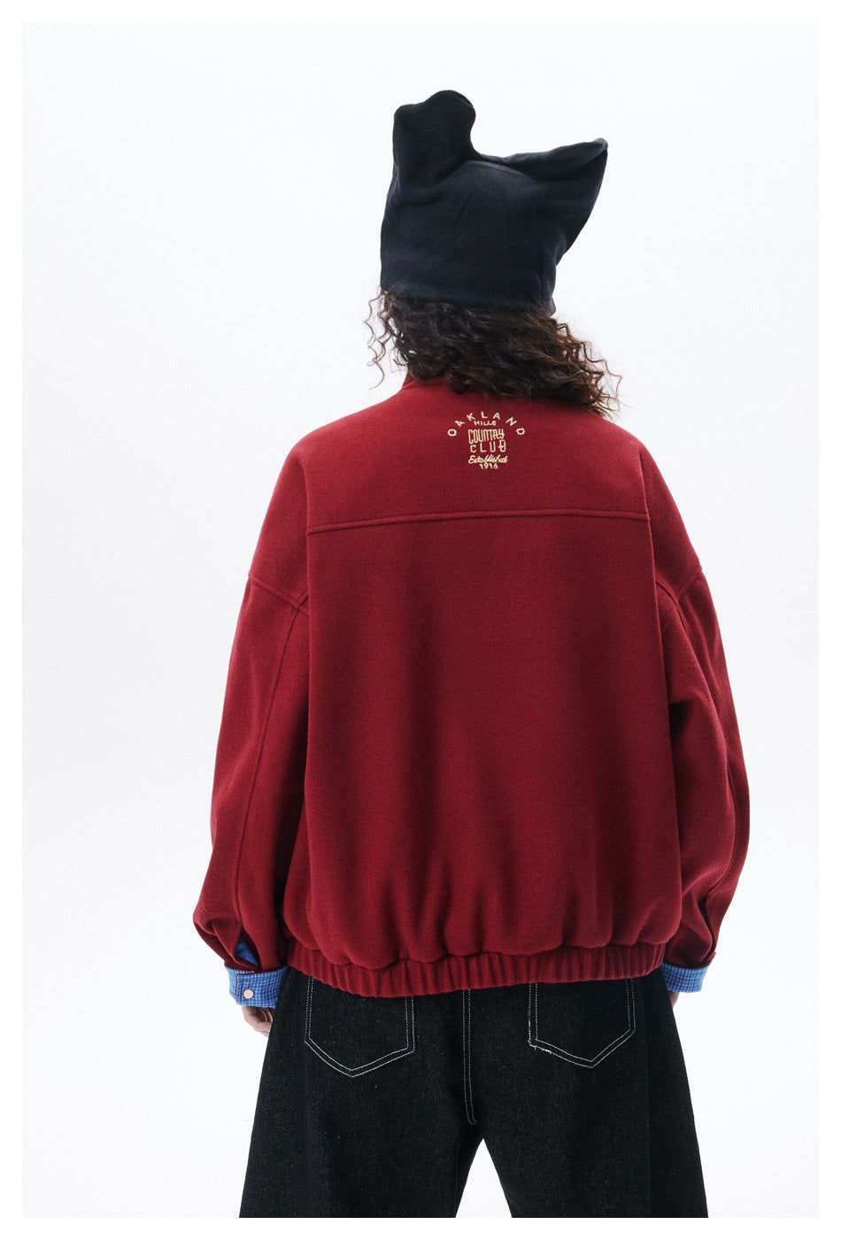 Close rear view of a model wearing a burgundy jacket with elastic hem and small upper-back embroidery.
