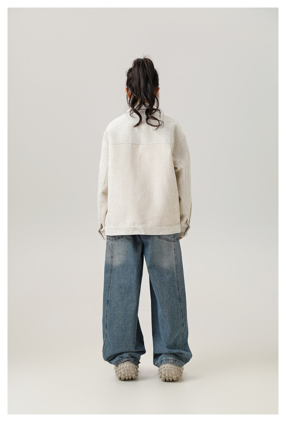 Rear view of a model wearing an ivory textured jacket with a plain back and loose blue jeans.
