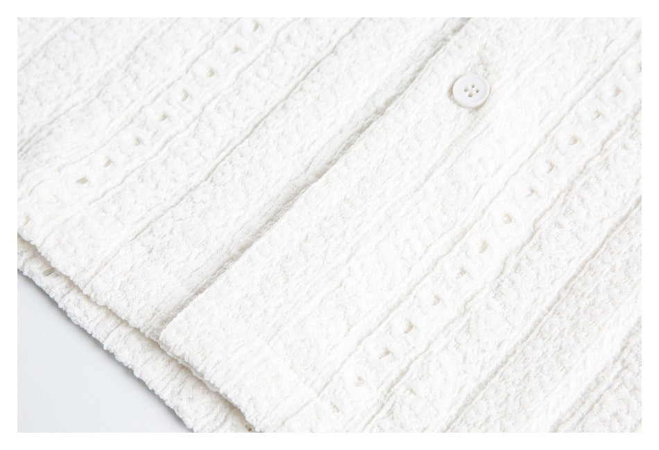 Close-up of a white shirt button, placket, and textured fabric with openwork stripes.