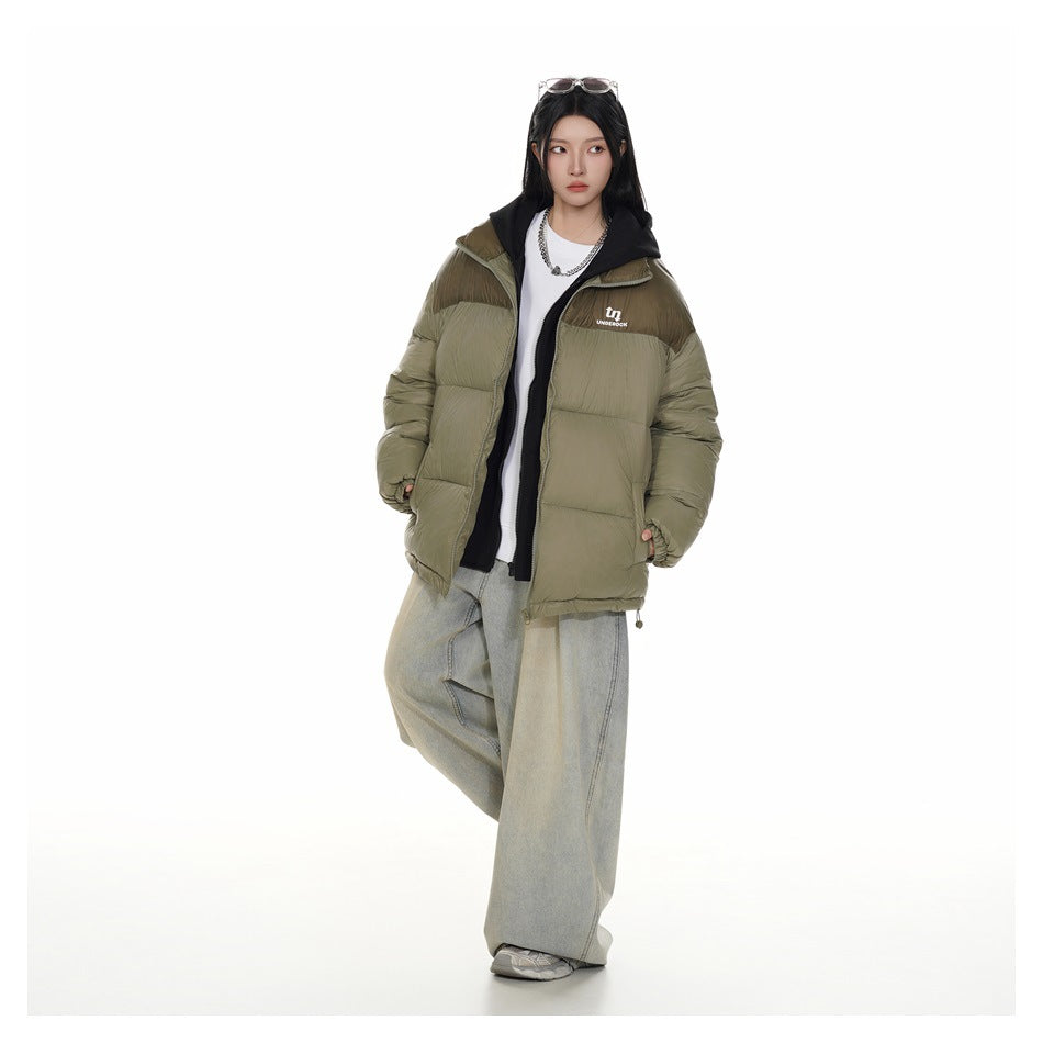 Full-length model wearing an open olive puffer jacket with a brown upper panel, black hood, and wide-leg light jeans.