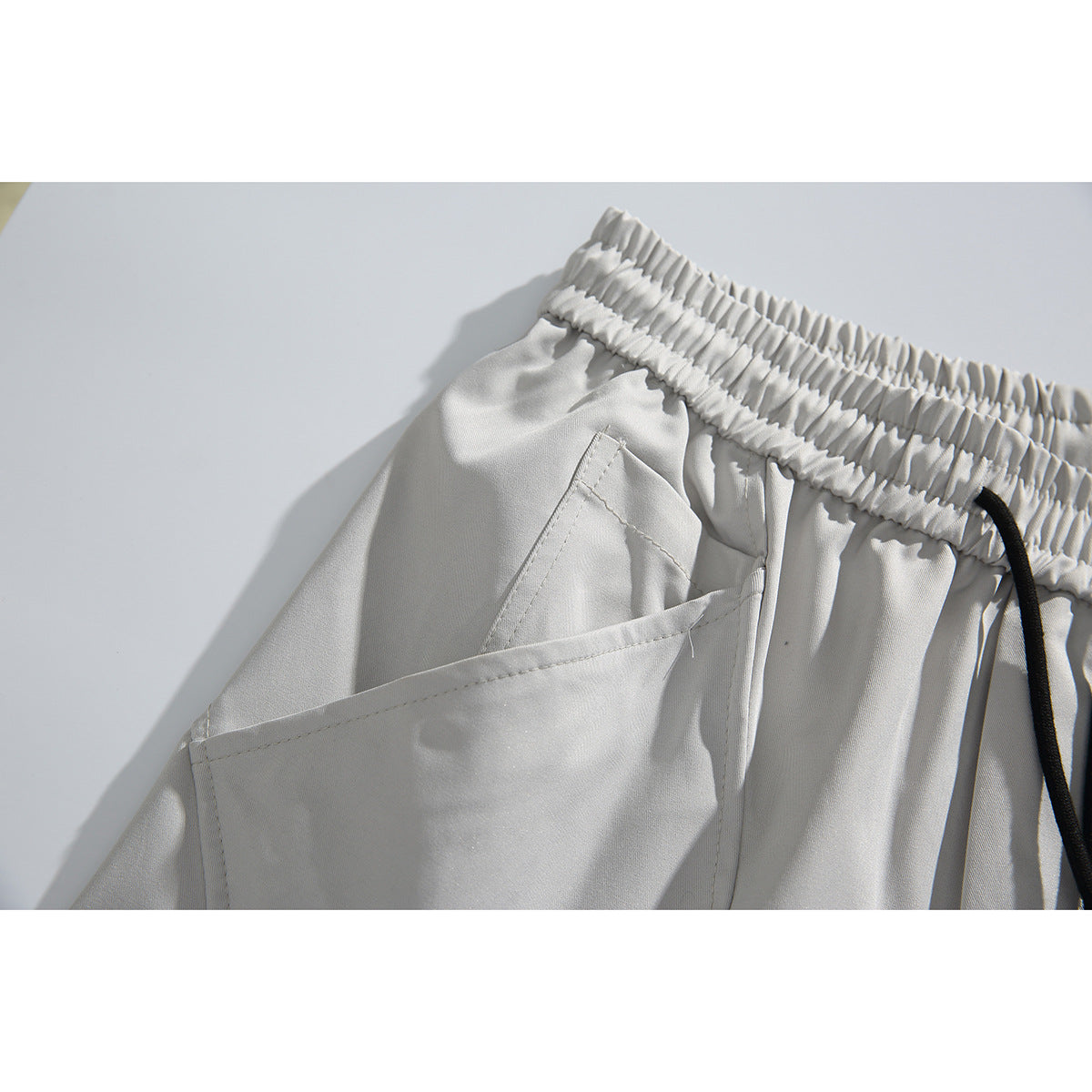 Close-up of light gray trousers showing the elastic waistband, black drawstring, and angled side pocket.