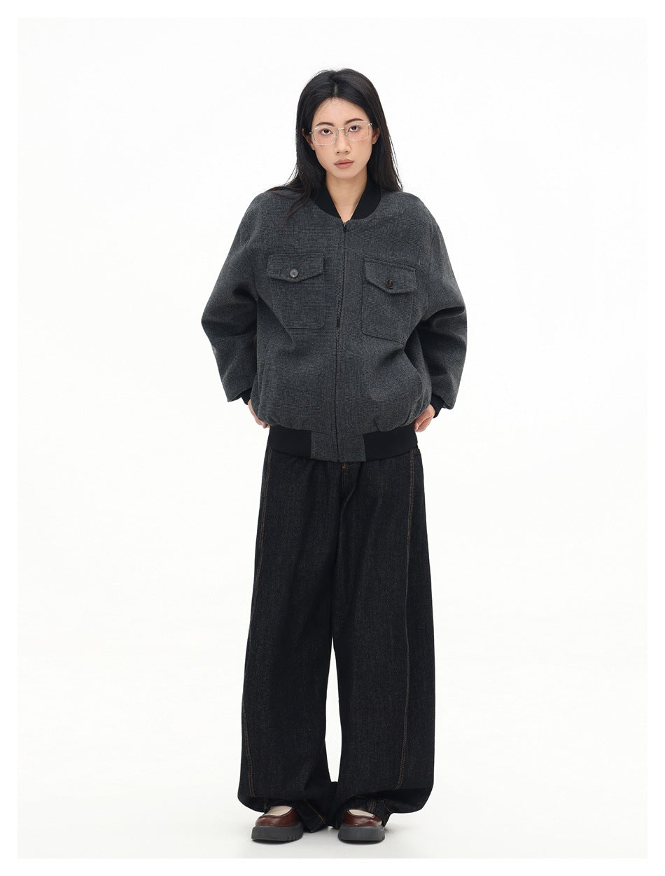 Full-length front view of a model in a charcoal gray plaid bomber jacket with black ribbed trim and wide-leg black jeans.
