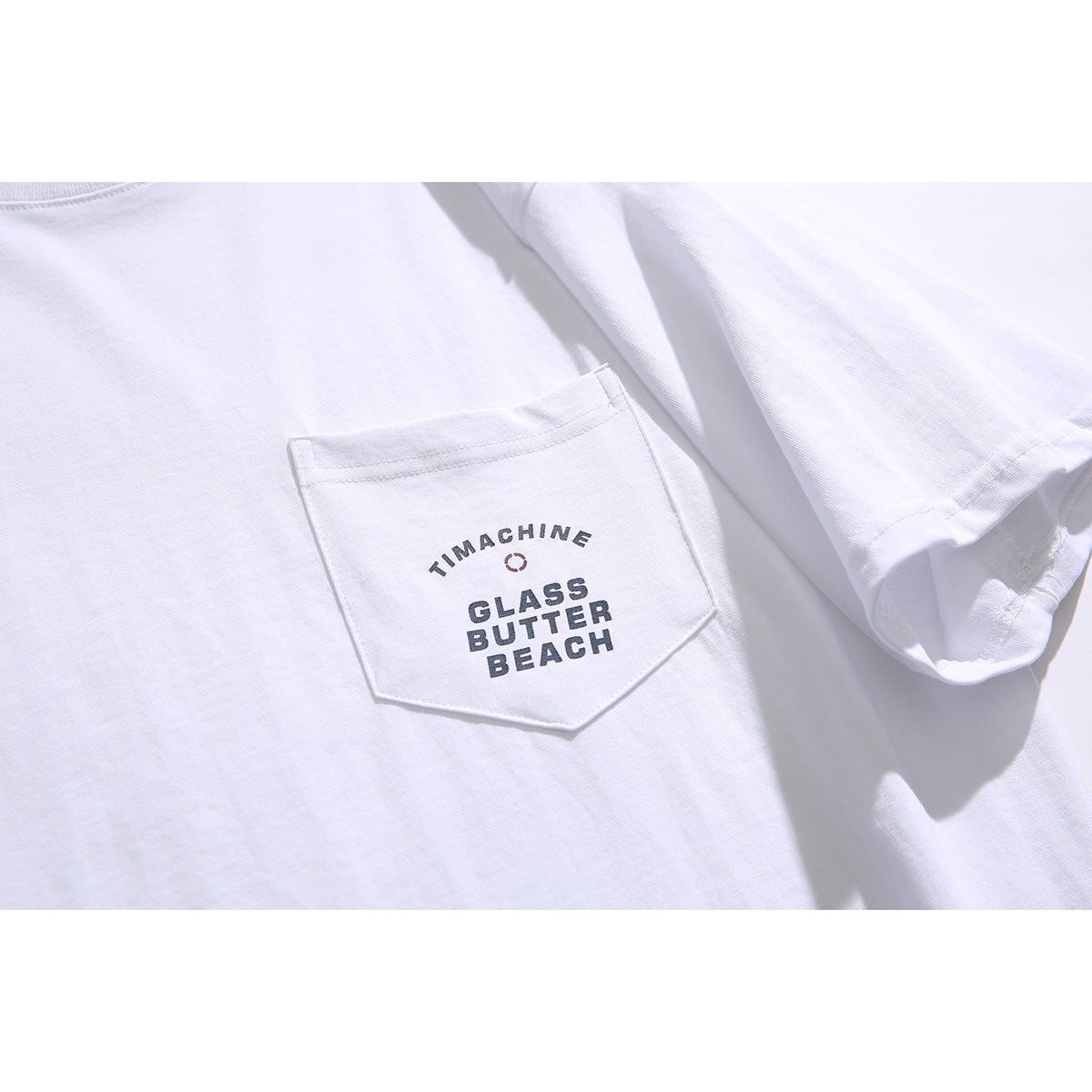 Close-up of a white T-shirt's chest pocket with dark printed text and a small circular graphic.
