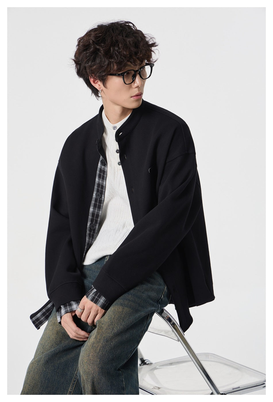 Model wearing a black stand-collar jacket with plaid inner placket and cuffs, layered over a white sweater.