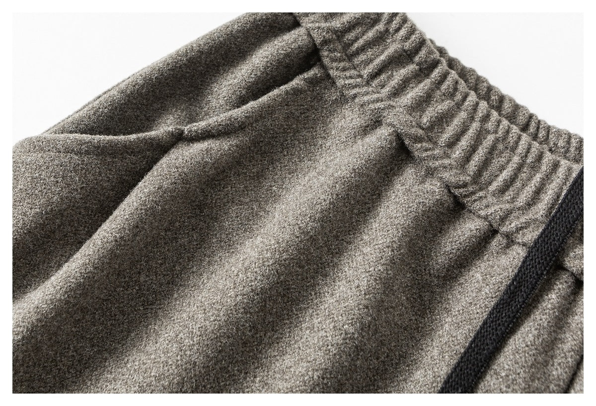 Angled close-up of gray pants showing the elastic waistband, front pleats, and a black drawstring.