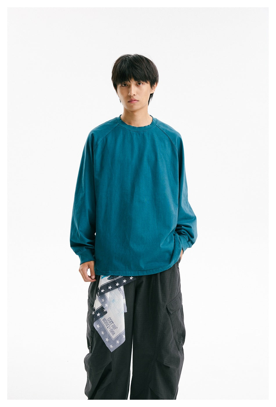 Front view of a model wearing a teal raglan long-sleeve shirt and dark cargo trousers.