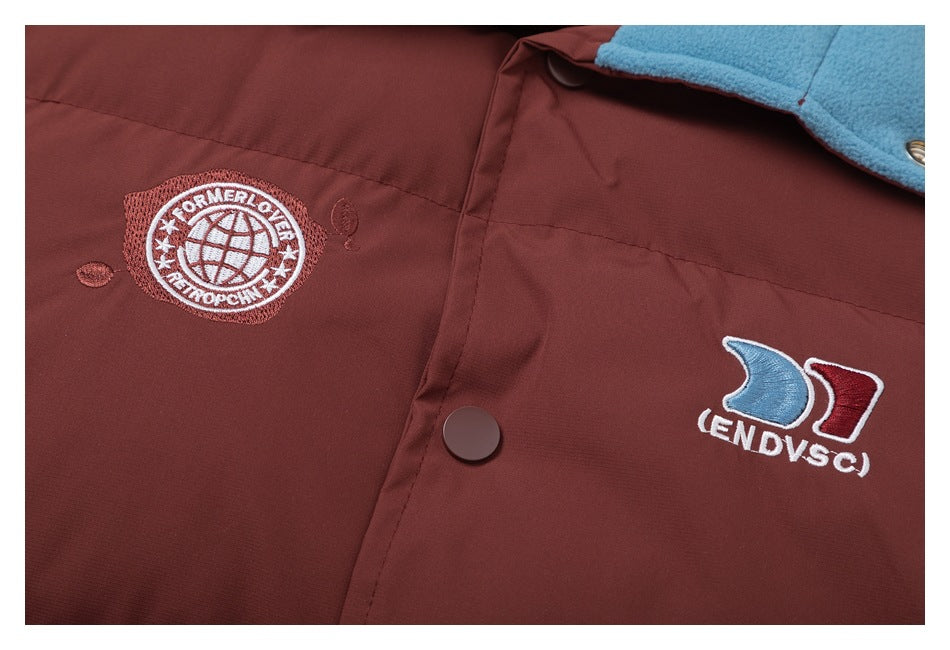 Close-up of two embroidered chest emblems and a snap closure on the burgundy jacket.